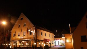 Un hôtel de style architectural européen traditionnel, caractérisé par une entrée imposante avec un auvent rouge et une enseigne indiquant la présence d’un restaurant.