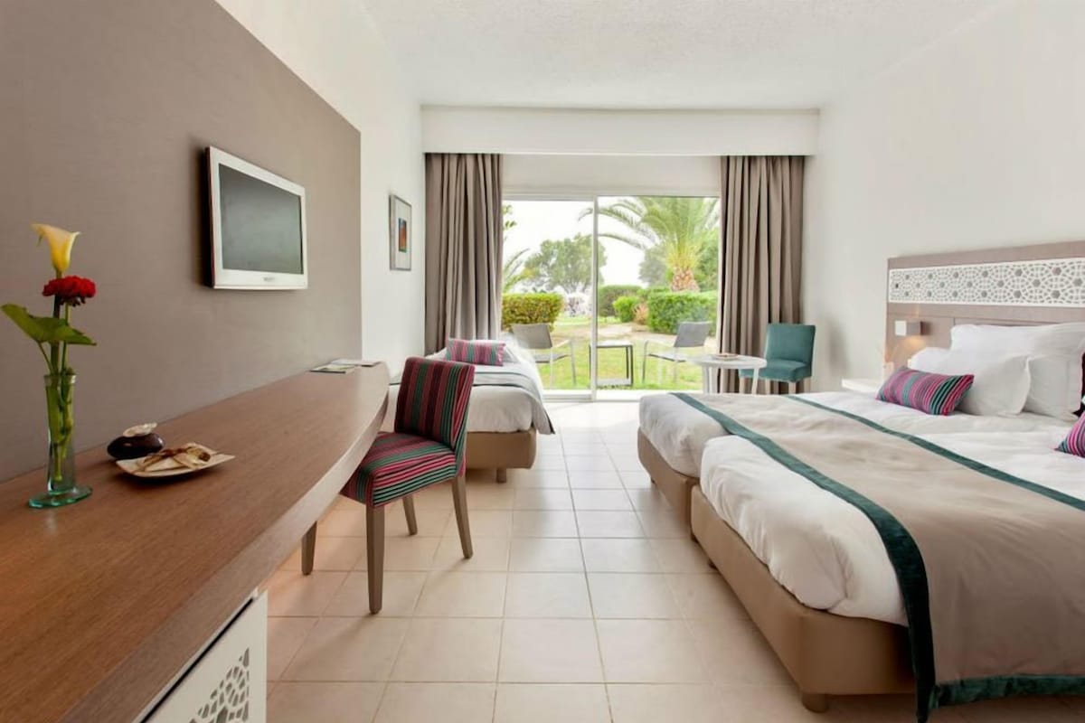 A hotel room with a bed, a desk, a chair, a TV, and a view of the outdoors.