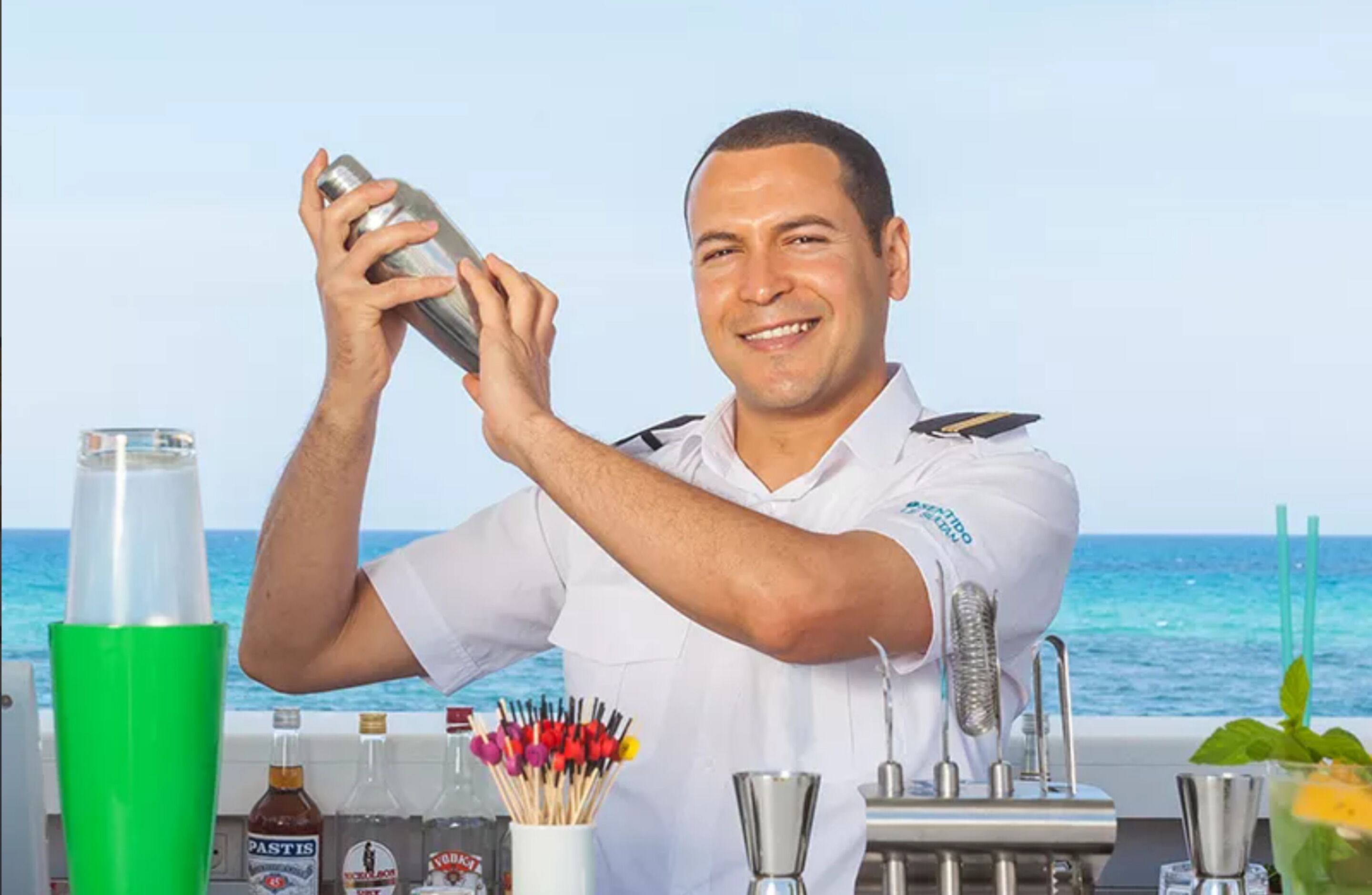 Un barman prépare un cocktail avec l’océan en toile de fond.