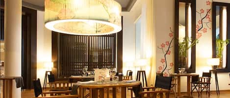 Comedor con mesas y sillas de madera, una lámpara colgante grande y decoración en las paredes.
