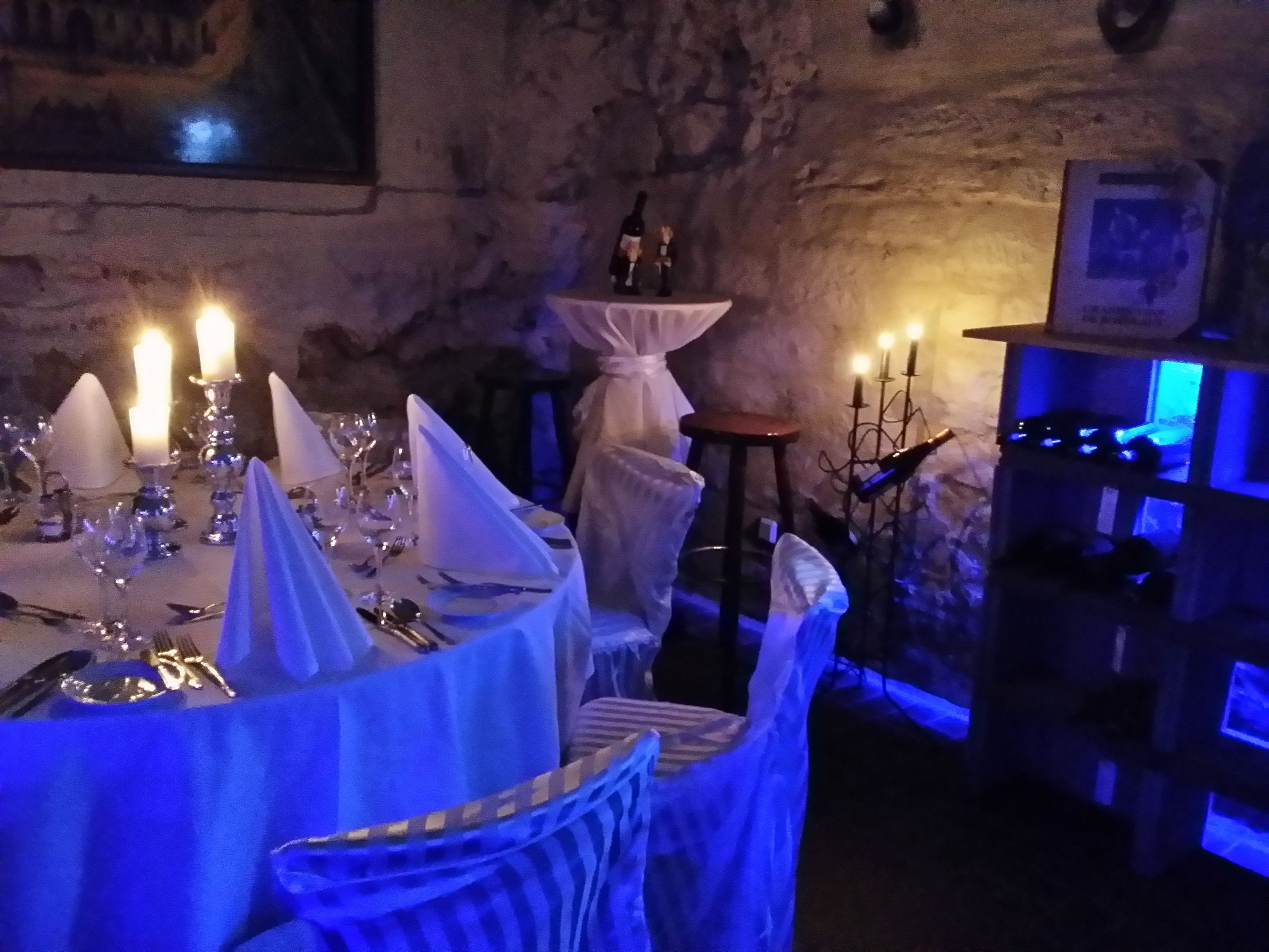 Un'area ristorazione scarsamente illuminata, con tavoli apparecchiati per un pasto, candele e una luce blu soffusa.