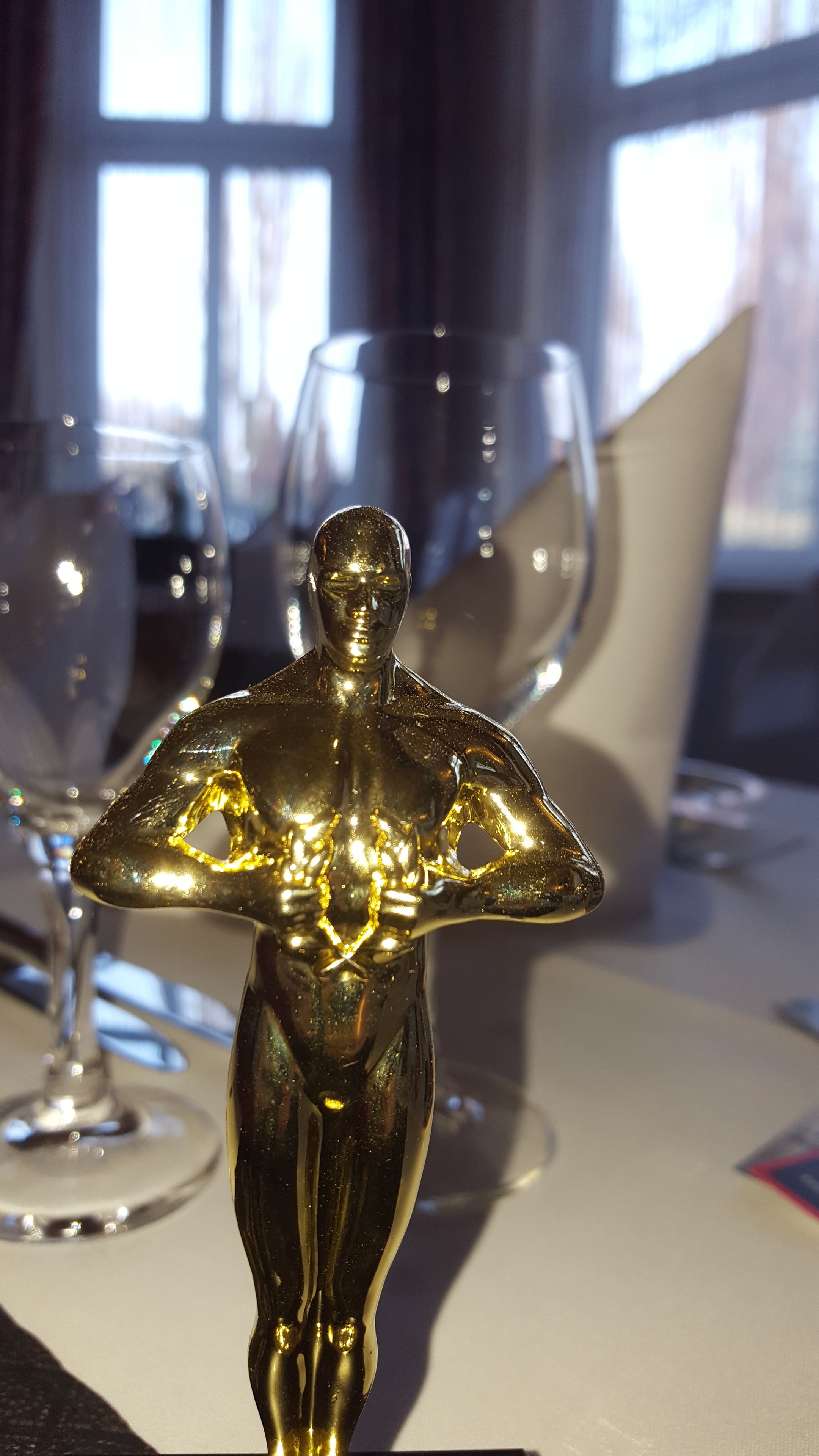 Une table ornée d’une statuette dorée, de verres à vin en verre transparent et d’une nappe blanche.