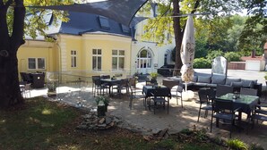 An outdoor patio area with tables and chairs, a stone fire pit, and a building with a yellow facade and a sign that reads "RESTAURANT IN WIPPER". - Hotel Wippertal (Ilberstedt)