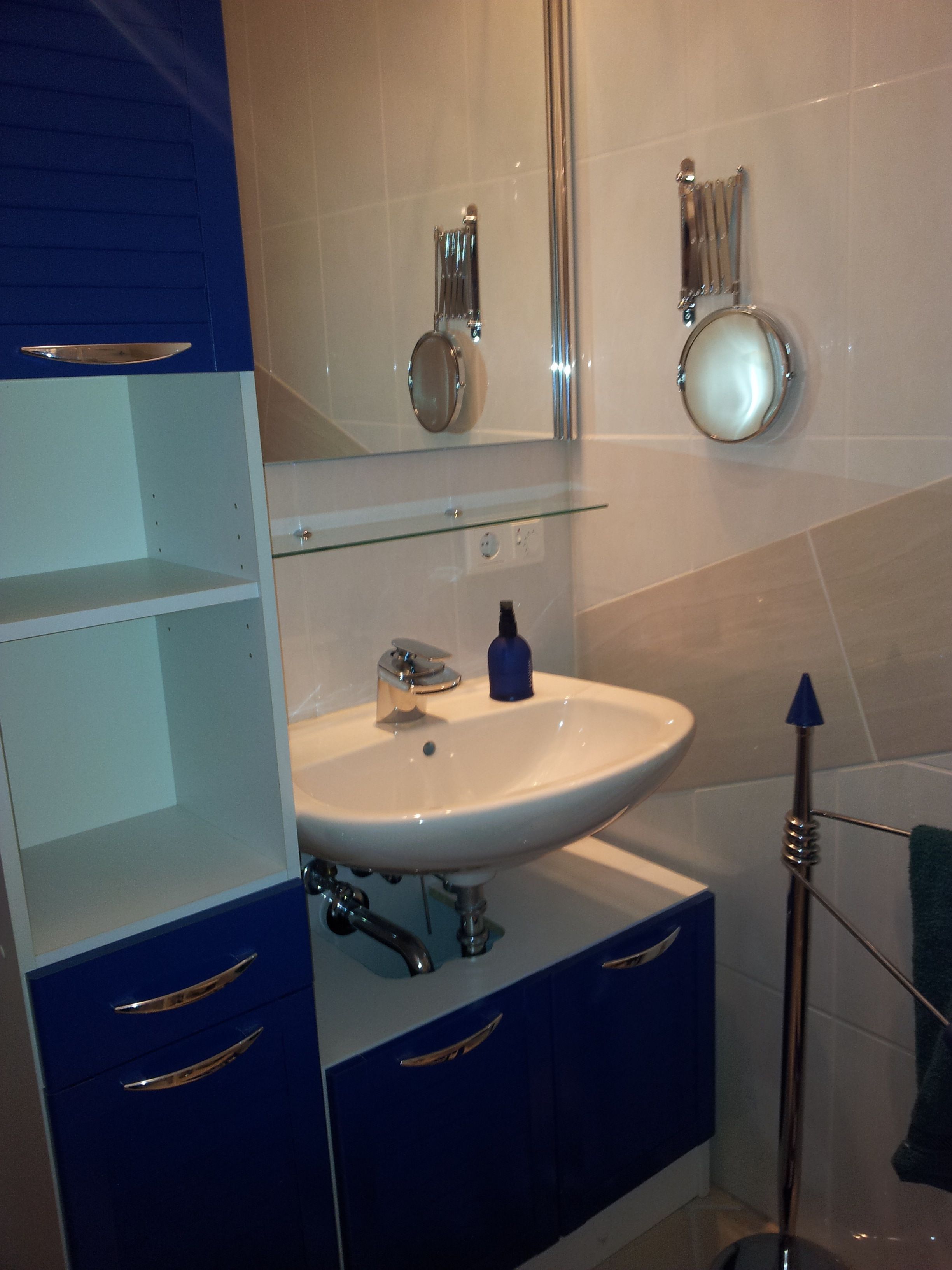 A bathroom with a white sink, blue cabinets, and a glass shelf.