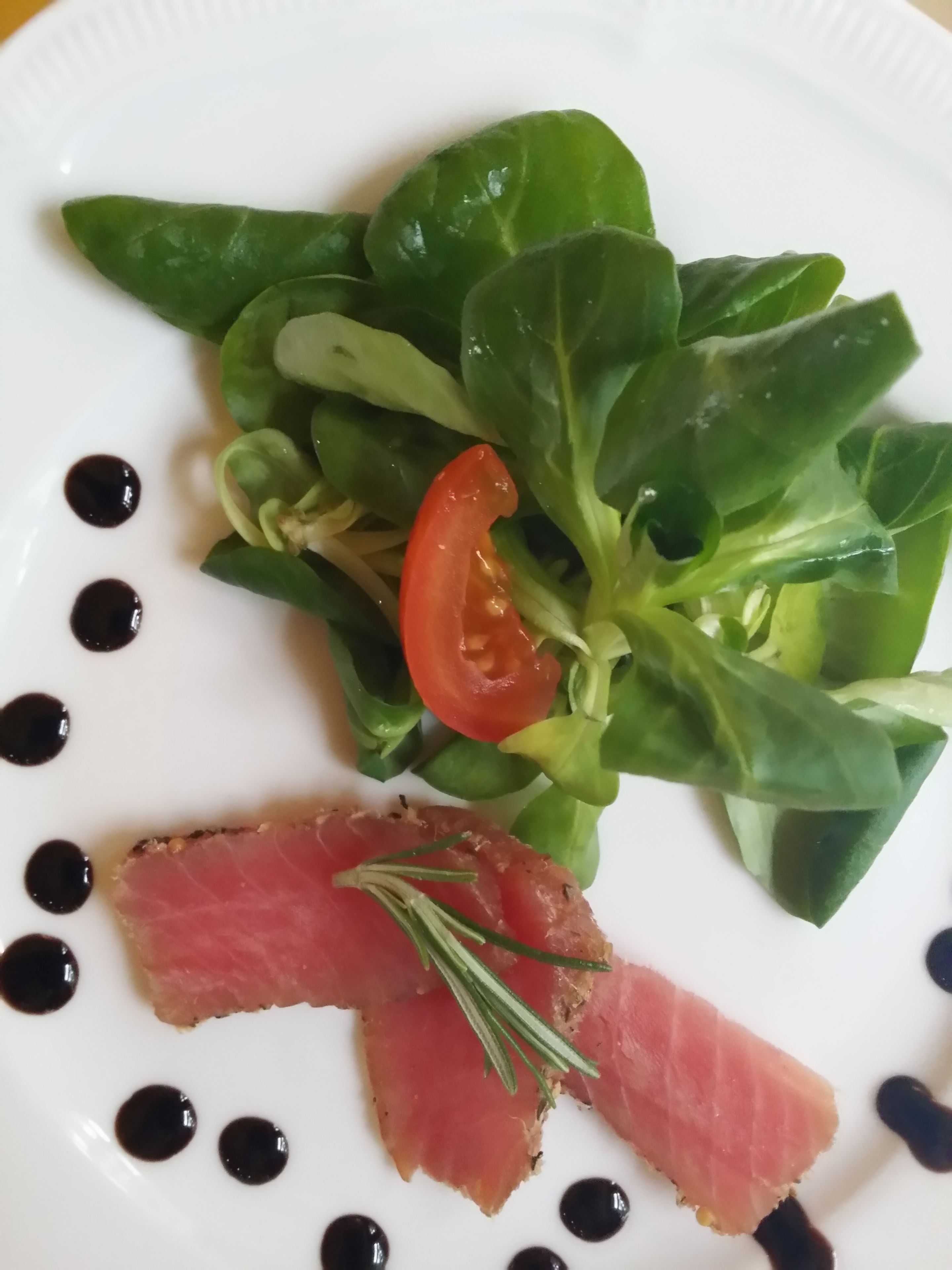 Un plato con ensalada, una porción de carne y puntos negros.