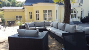 A modern outdoor seating area with a large sectional sofa and two armchairs, a dining table, and chairs, set against a yellow building with a dark roof. - Hotel Wippertal (Ilberstedt)