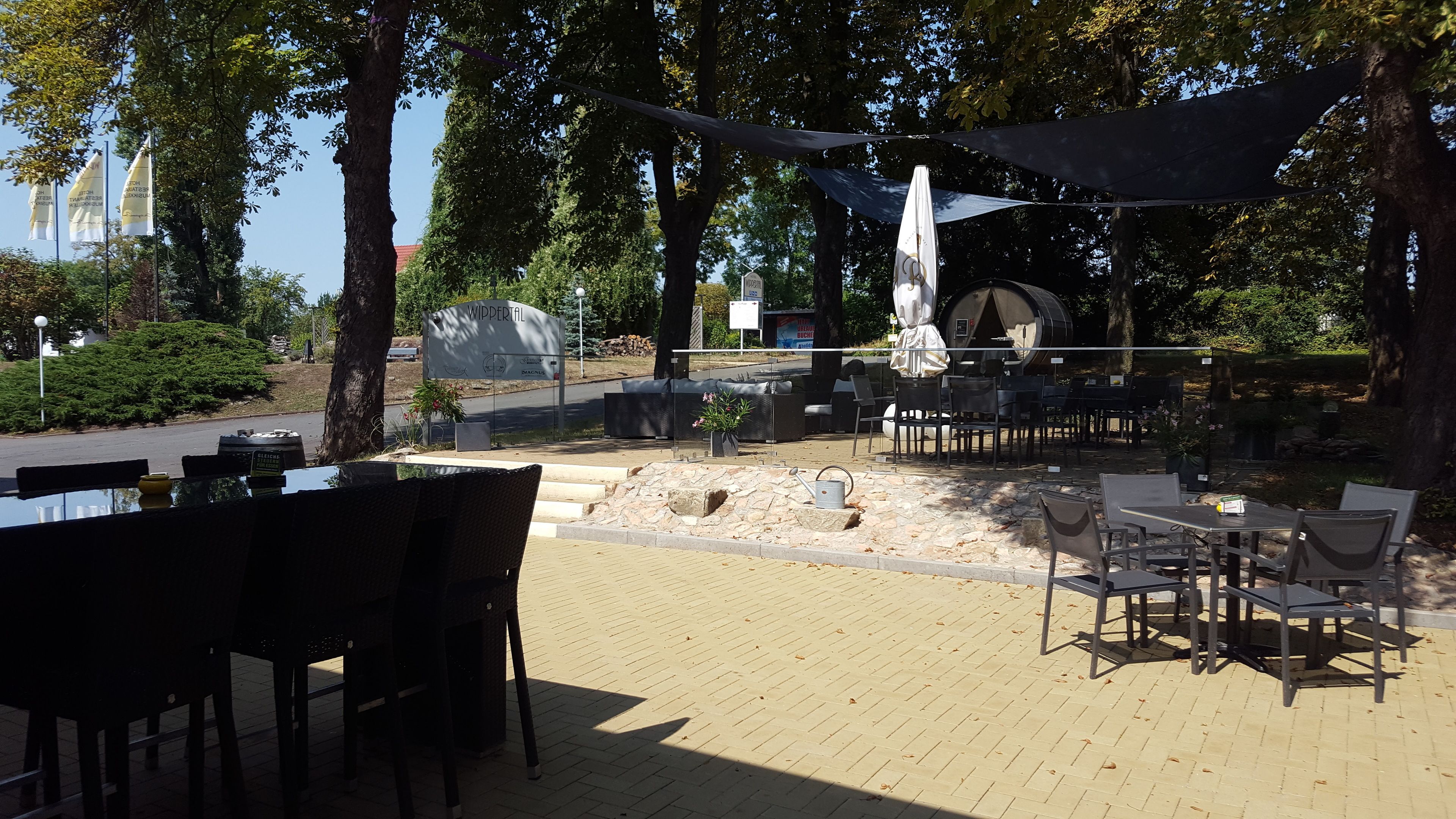 Un espace extérieur aménagé avec des tables et des chaises, un chemin en pierre et une enseigne indiquant « WIPPERTAL ».