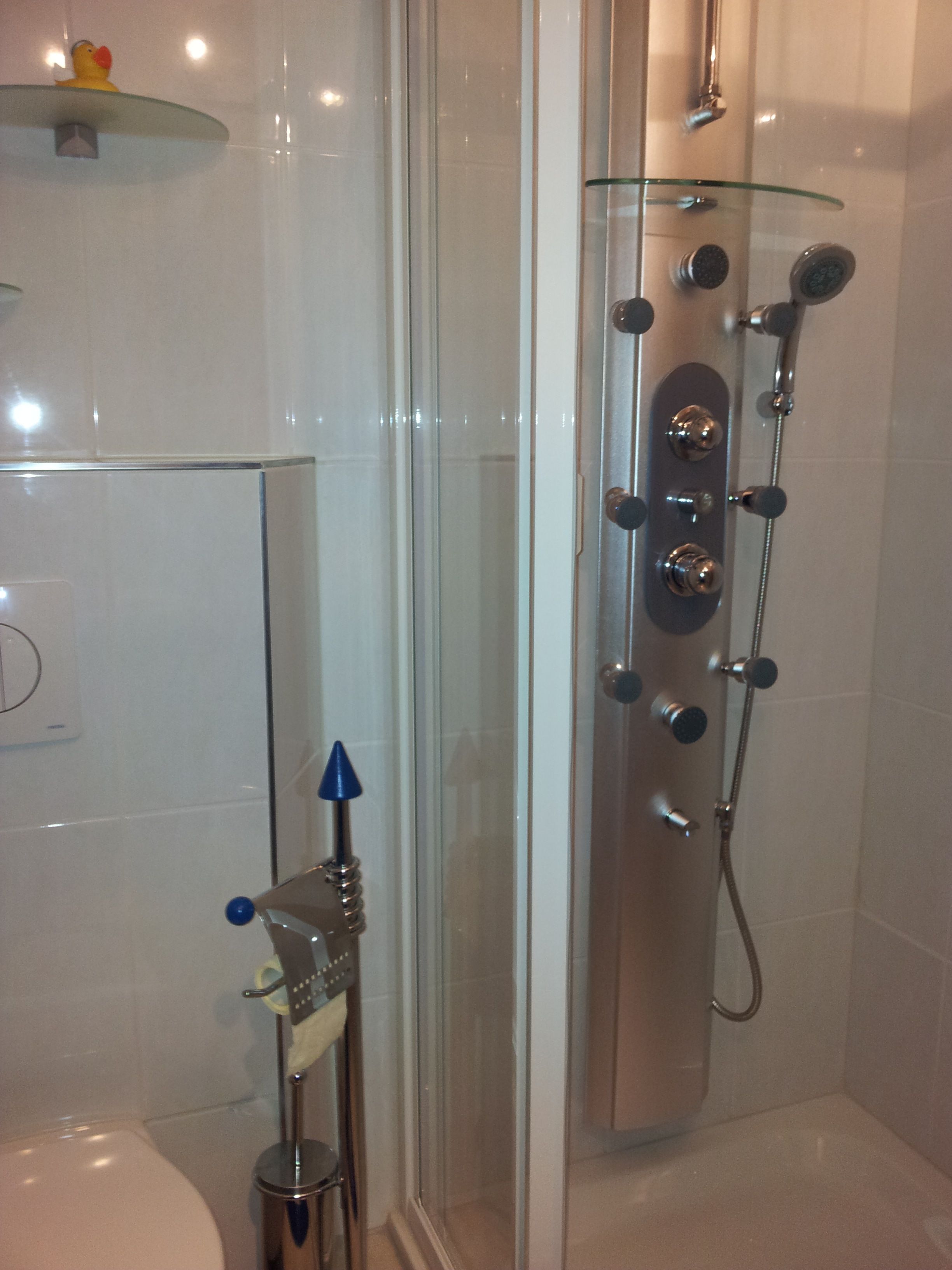 A bathroom with a glass shower enclosure, a toilet, and a glass shelf with a rubber duck.