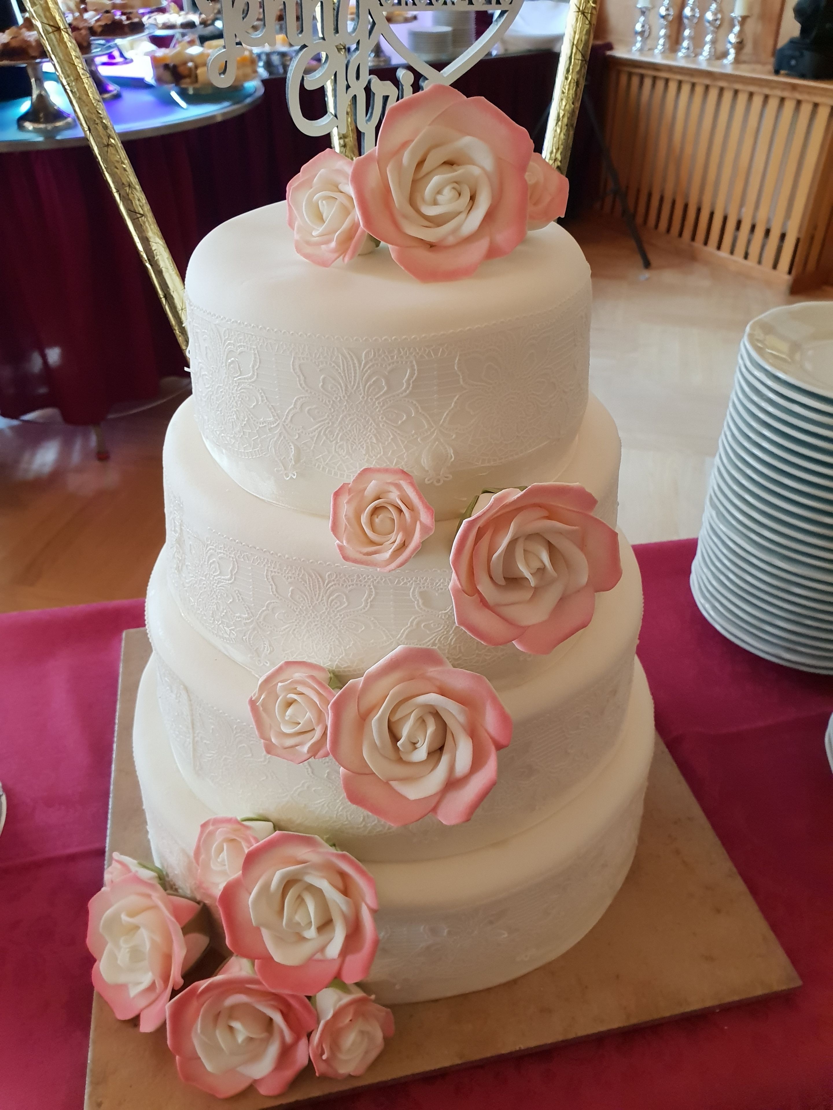 Un pastel de varios niveles con rosas rosadas y blancas en la parte superior, sobre una mesa con mantel rojo.