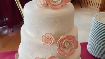 Un pastel de varios niveles con rosas rosadas y blancas en la parte superior, sobre una mesa con mantel rojo.
