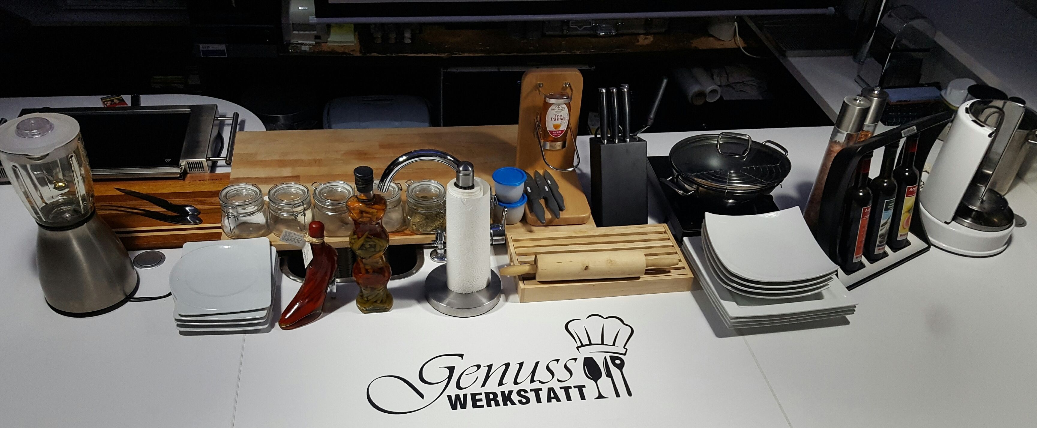Uma bancada de cozinha com diversos utensílios, uma cafeteira e uma placa com a inscrição 