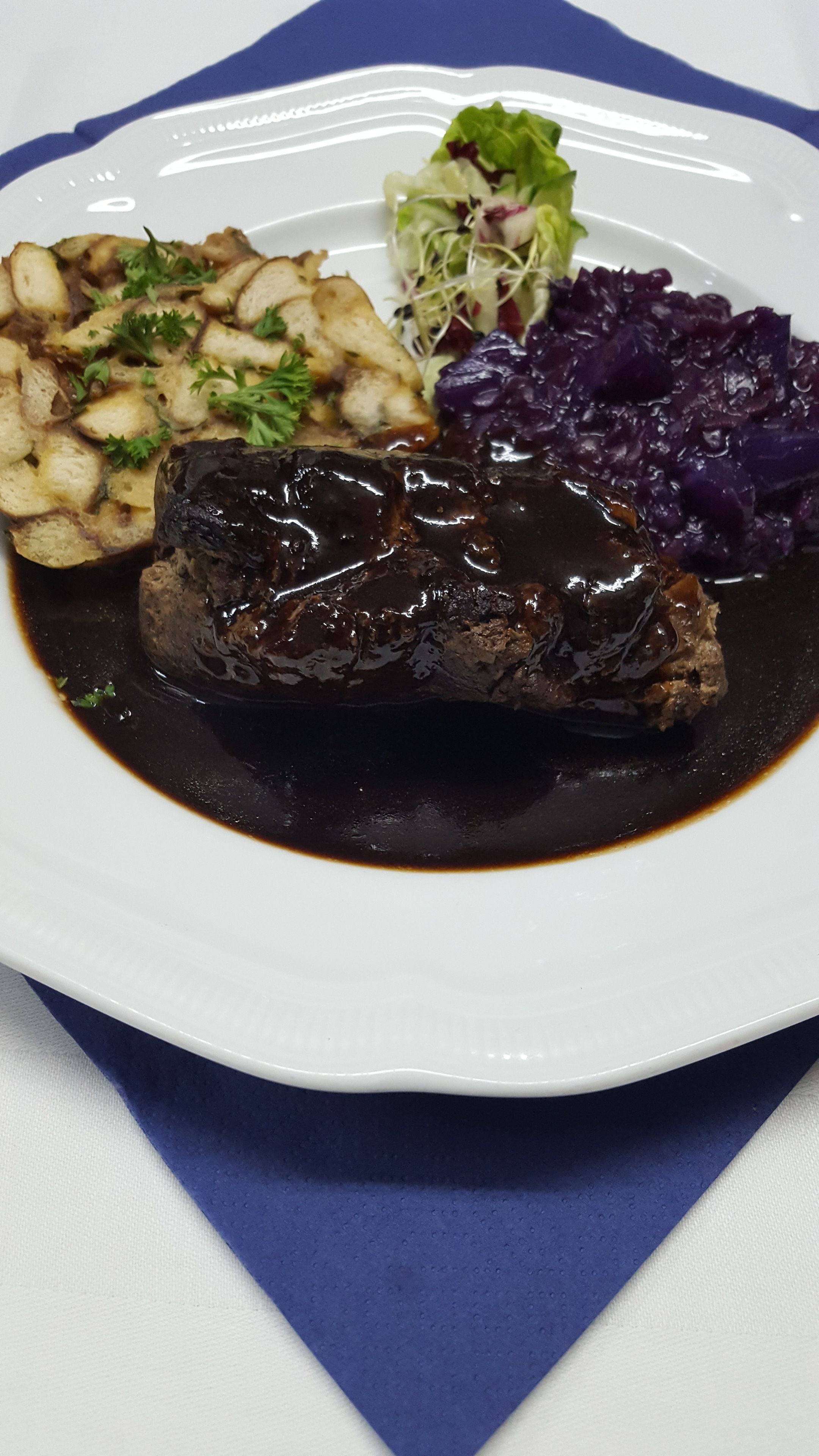 Une assiette contenant un plat de viande, des pommes de terre rôties et du chou rouge.
