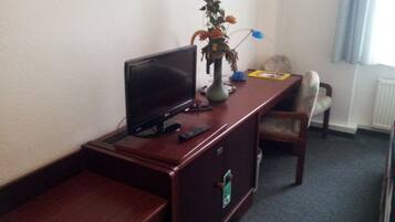 Une chambre d’hôtel avec un bureau en bois, une télévision, un vase de fleurs, une télécommande et une chaise.