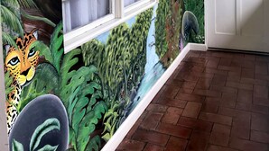 Una habitación con un mural de aves y follaje en la pared, una ventana con marcos blancos y una puerta con el número 10.