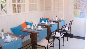 Comedor con mesas dispuestas para dos, con manteles azules y vajilla blanca.