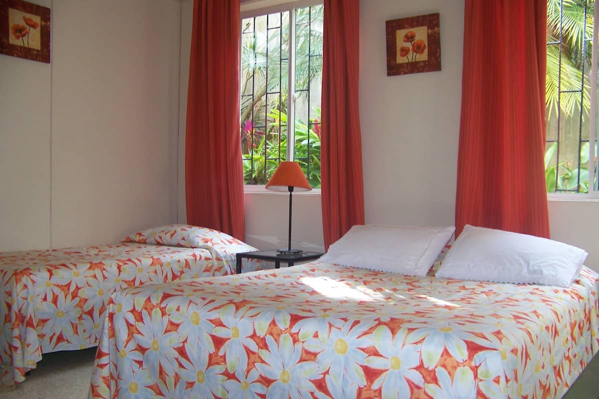 Ein Hotelzimmer mit zwei Betten, roten Vorhängen, einem Fenster mit Blick ins Grüne und einer Lampe auf einem Nachttisch.