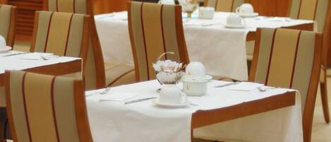 Un comedor con mesas dispuestas para el servicio, sillas con tapicería a rayas y un bufé al fondo.