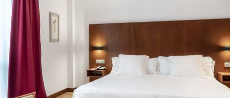 A hotel room with a large bed, wooden headboard, two bedside tables with lamps, a red curtain, and a framed picture on the wall.
