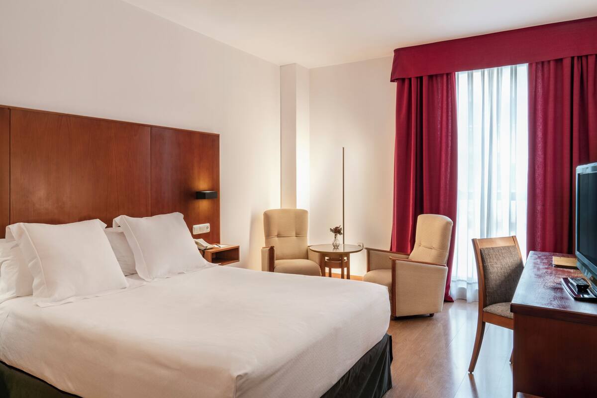 A hotel room with a large bed, two armchairs, a desk, and a television.