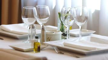 A table set with wine glasses, plates, and cutlery, with a vase of flowers and a salt and pepper shaker.