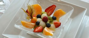 Een vierkant glazen bord met een fruitsalade op een witte dienblad.