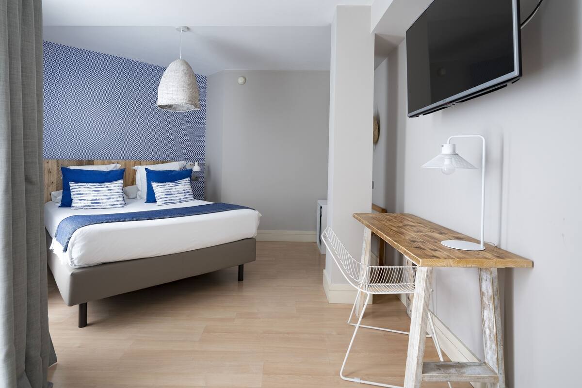 A modern bedroom with a bed, a desk, a TV, and a patterned wall.