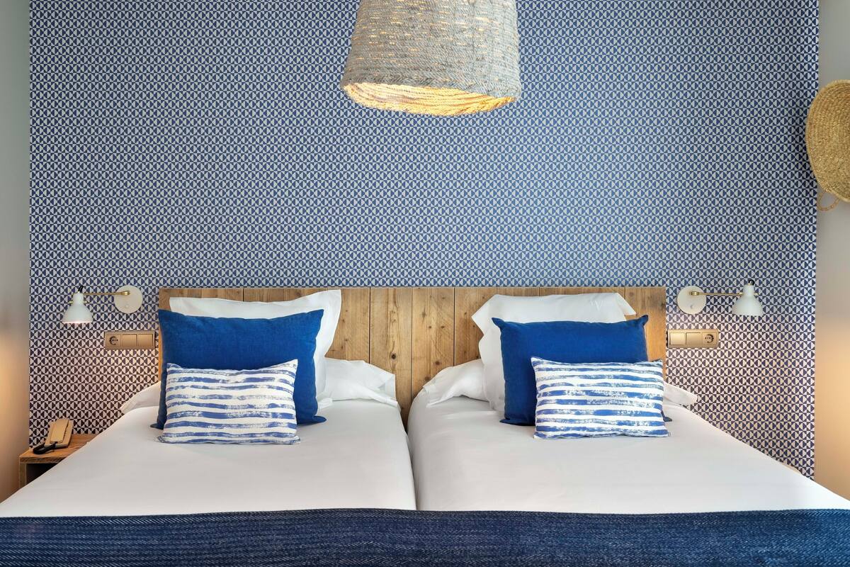 A double bed with white and blue bedding, two blue pillows, and a wooden headboard.