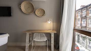 Una habitación con un escritorio de madera, una silla blanca, un televisor montado en la pared y dos cestas tejidas.