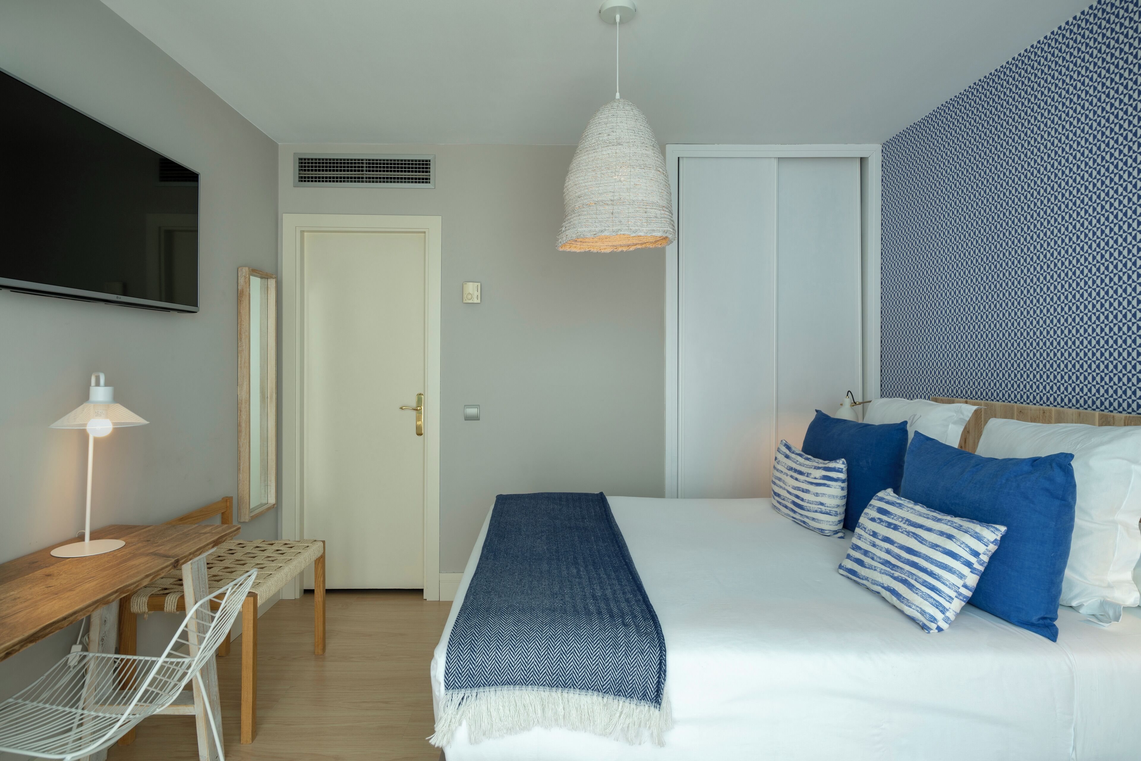 A bedroom with a bed, bedside table, lamp, and a TV mounted on the wall.