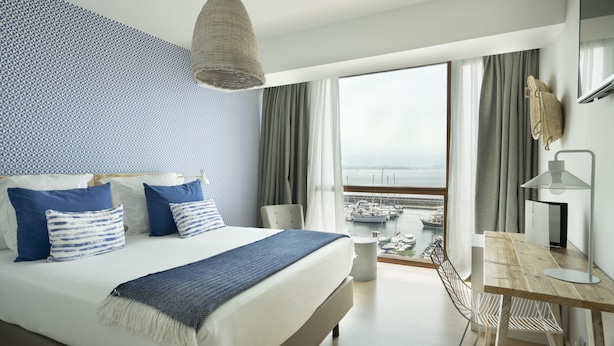 A modern hotel room with a large bed, a desk, and a view of the marina. - Hotel Vincci Puertochico (Santander)