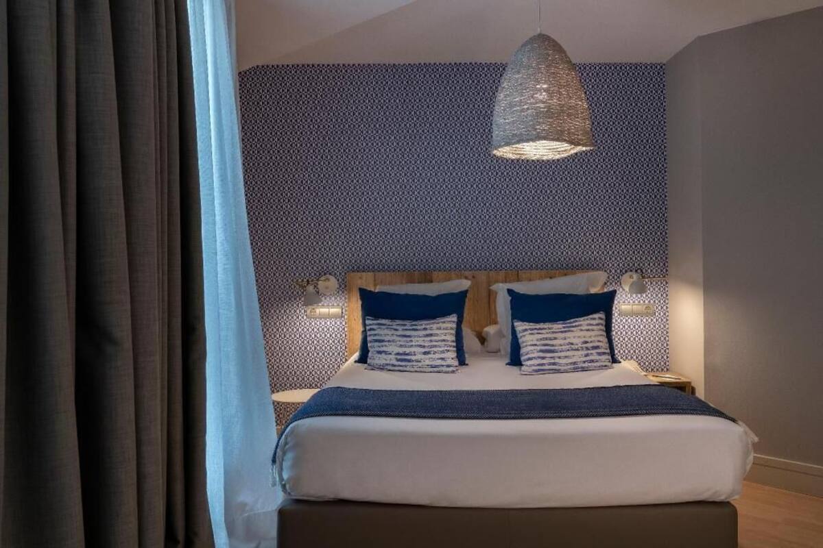 A bedroom with a bed, a hanging light fixture, and patterned wallpaper.