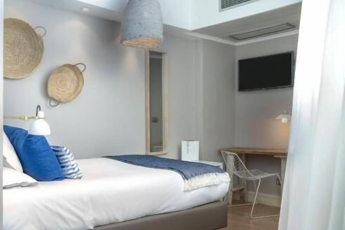 A bedroom with a bed, bedside lamp, wall-mounted basket, and a desk with a chair.