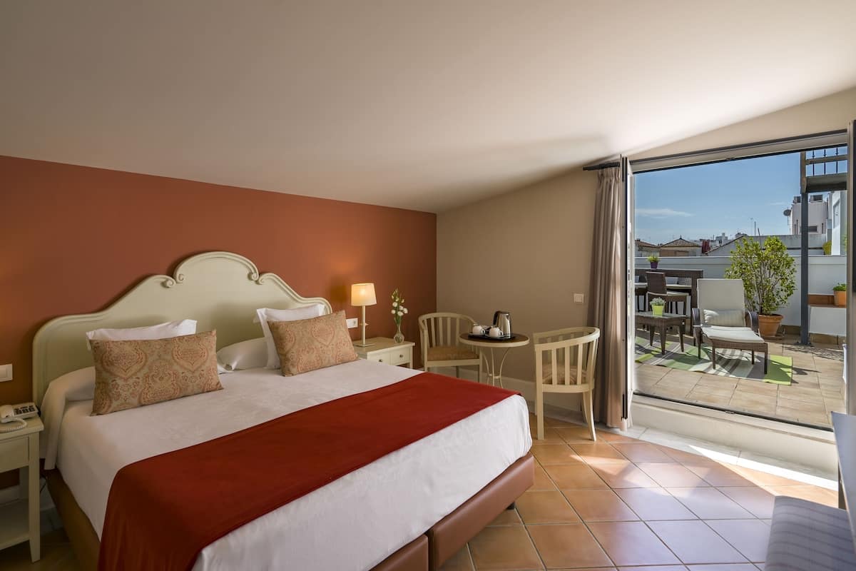 A hotel room with a large bed, a small table with chairs, and a balcony with a view of buildings.