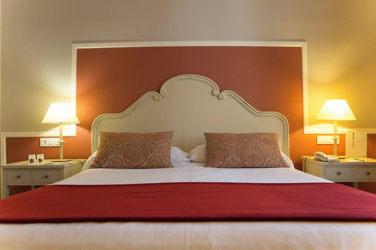 A hotel room with a large bed, two bedside tables with lamps, a telephone, and a minibar.