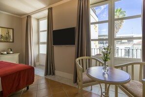 Habitació d'hotel amb un llit, una taula petita amb un vas, una televisió penjada a la paret i una finestra amb cortines.