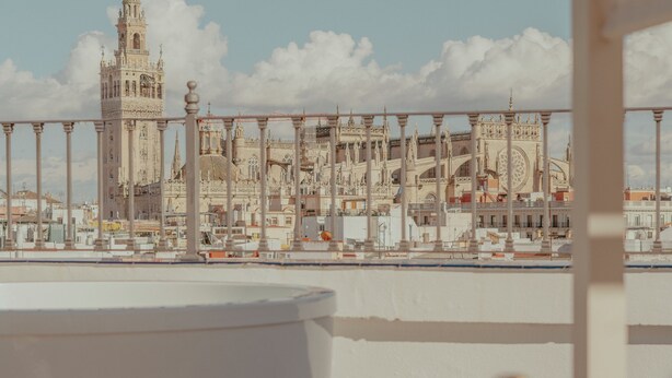 Een balkon met uitzicht op een historische kathedraal, een witte zithoek en een fles champagne.