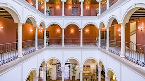 Een meerlaags atrium met boogvormige loopbruggen en balkons, met een open centrale ruimte met zitplaatsen en beplanting.