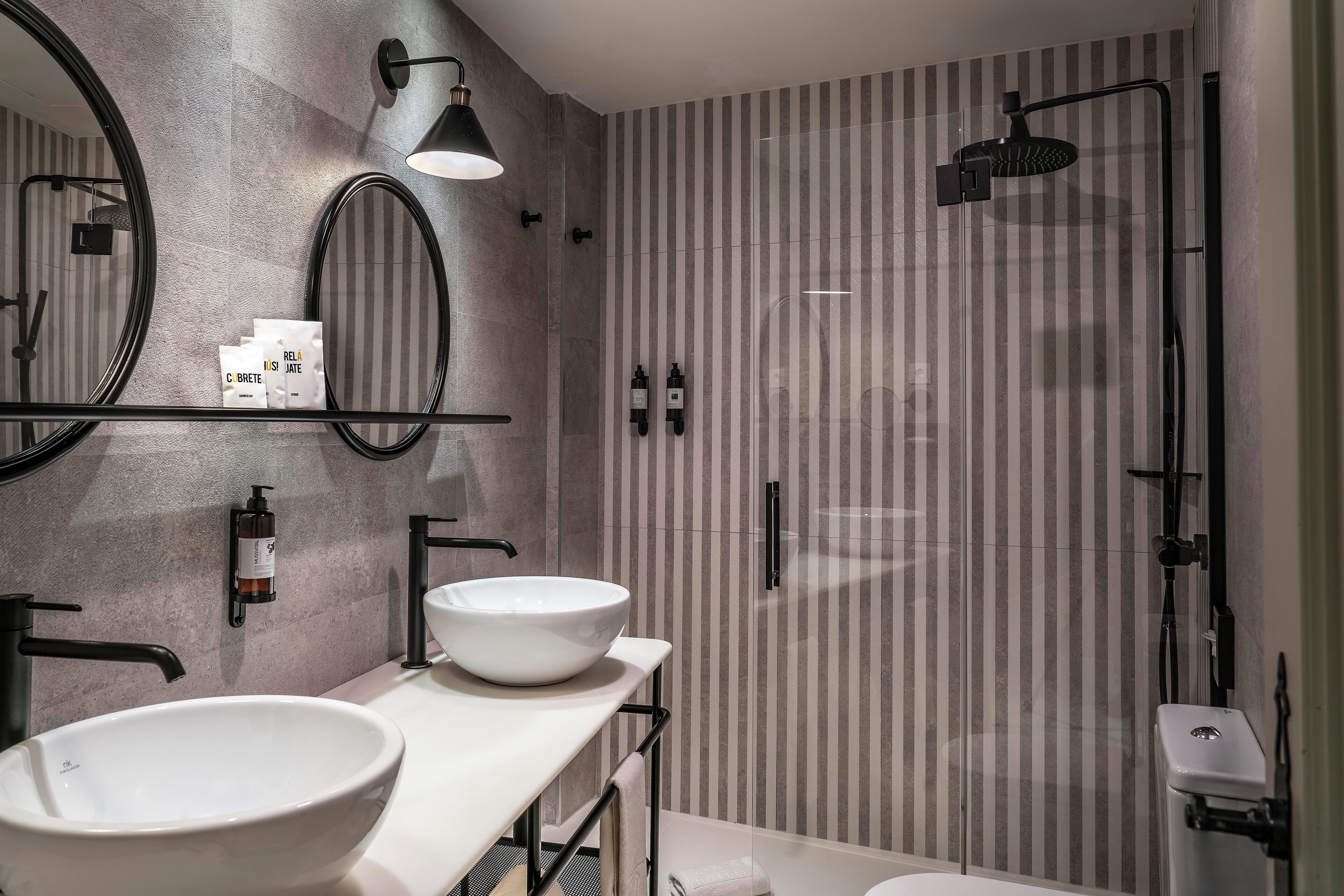 Un baño moderno con un espejo redondo grande, un lavabo blanco y una zona de ducha.