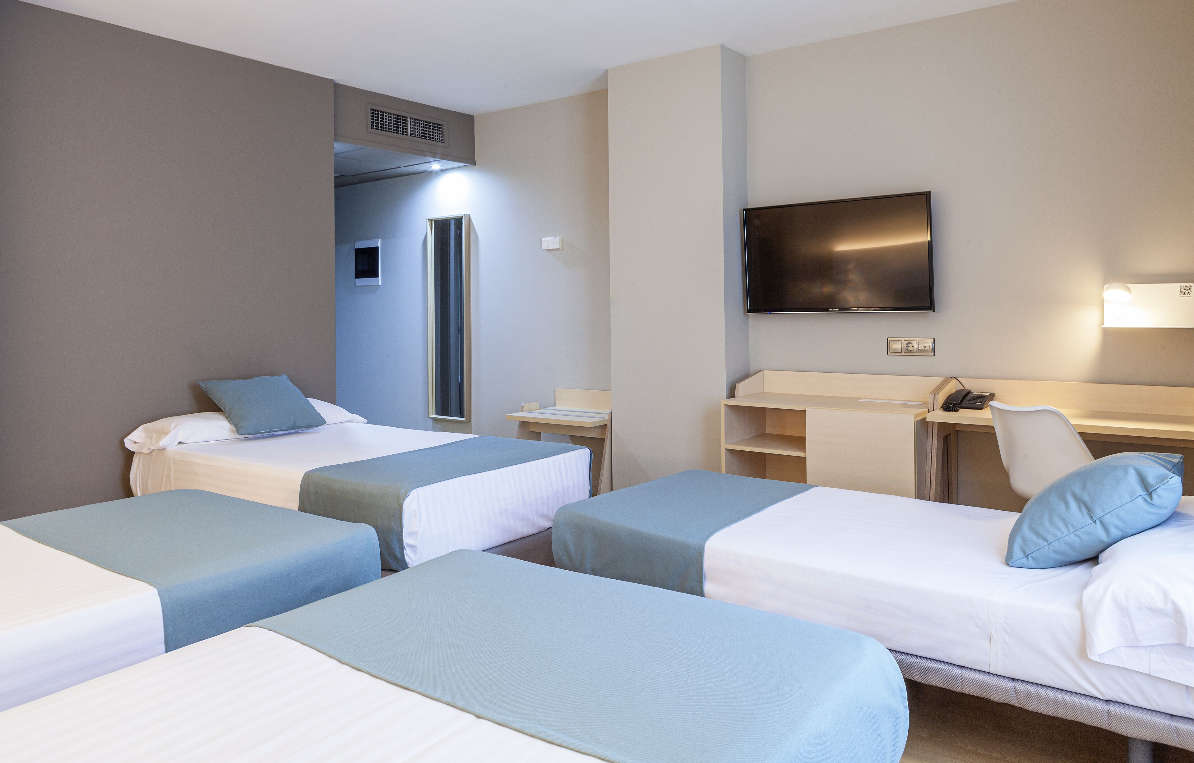 Una habitación de hotel con dos camas individuales, un escritorio, una silla, un televisor y un minibar.