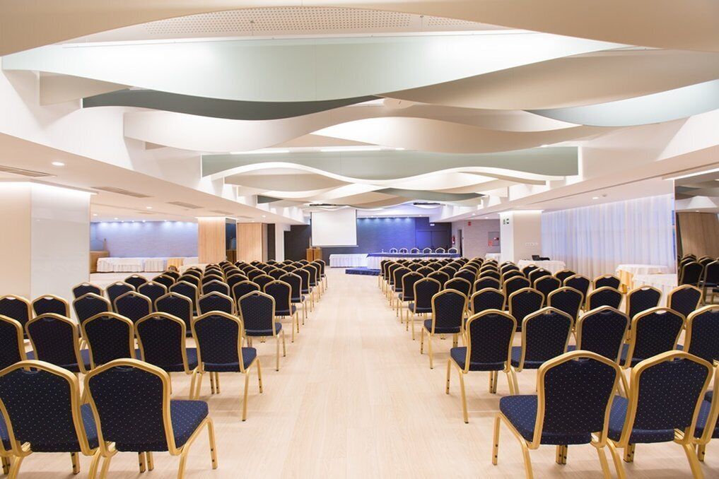 Un salón de conferencias con filas de sillas y un escenario al frente.
