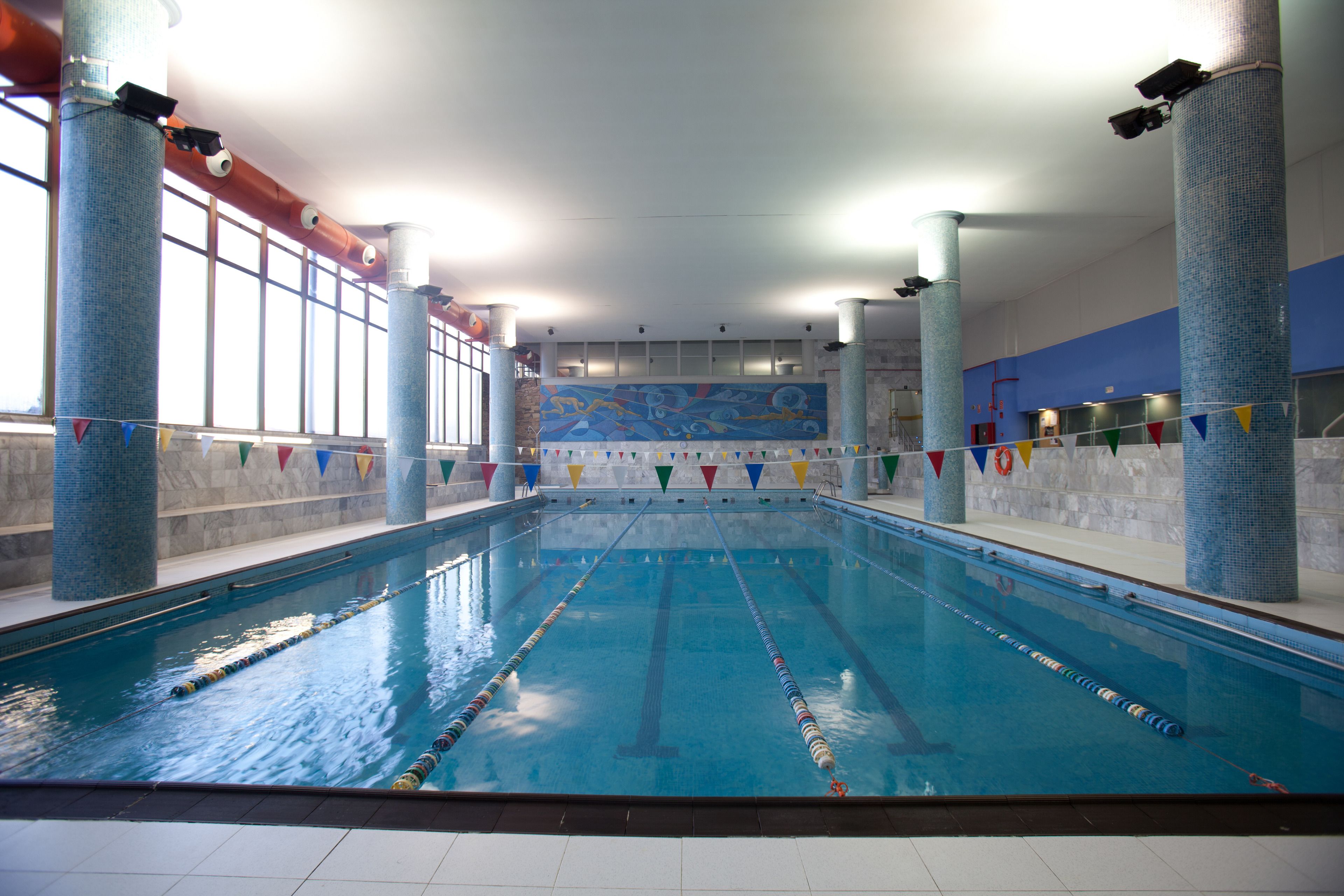 Una piscina interior amb carrils ben definits, grans finestres i parets de rajola blava.