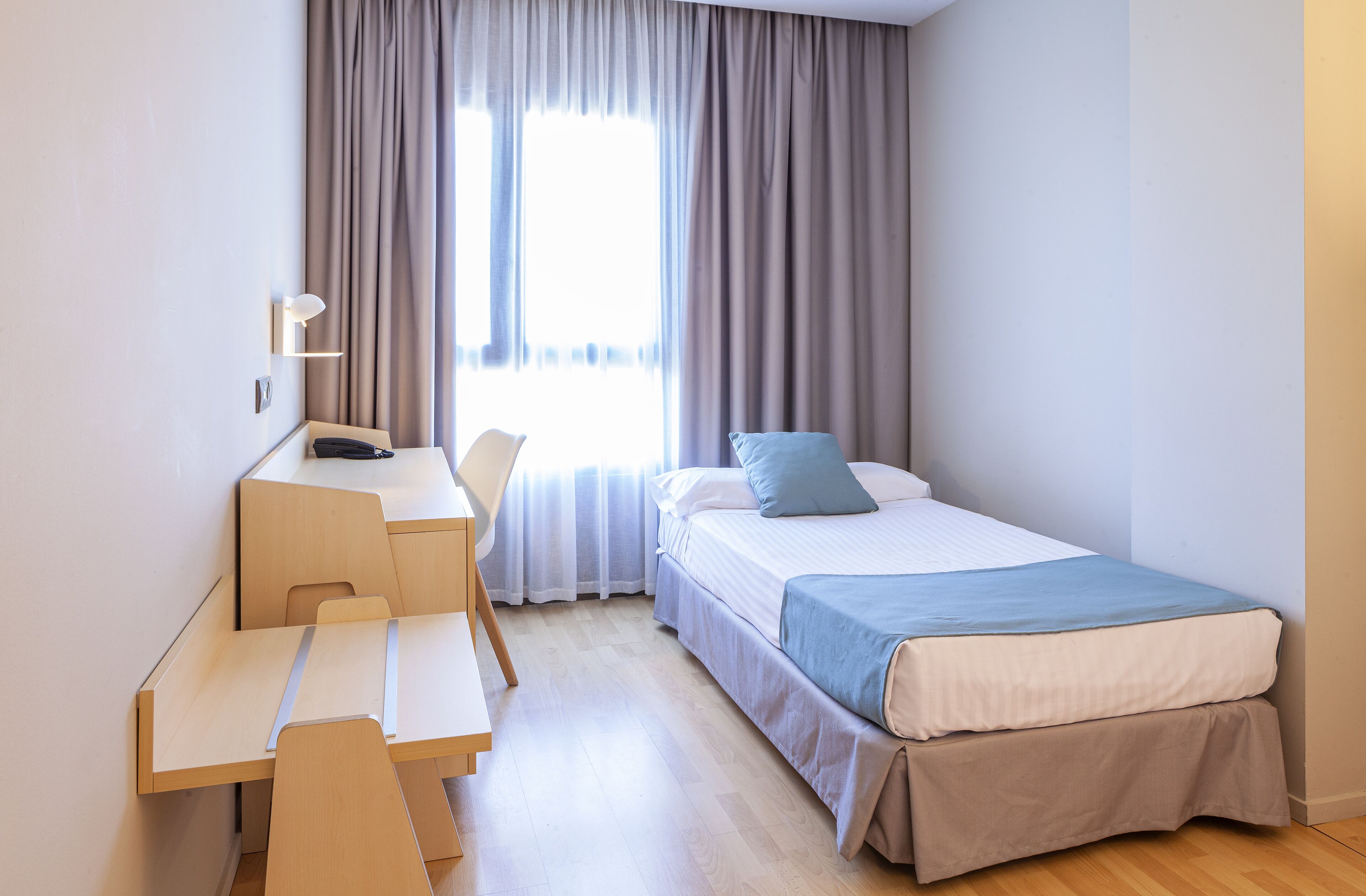 Een ruime, goed verlichte kamer met een bed, een bureau en een stoel.