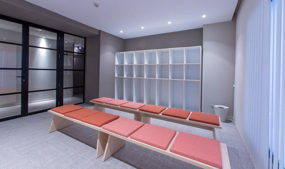 Un área de espera moderna con un mostrador de recepción, una zona de estar con bancos acolchados y un mueble de almacenamiento empotrado.
