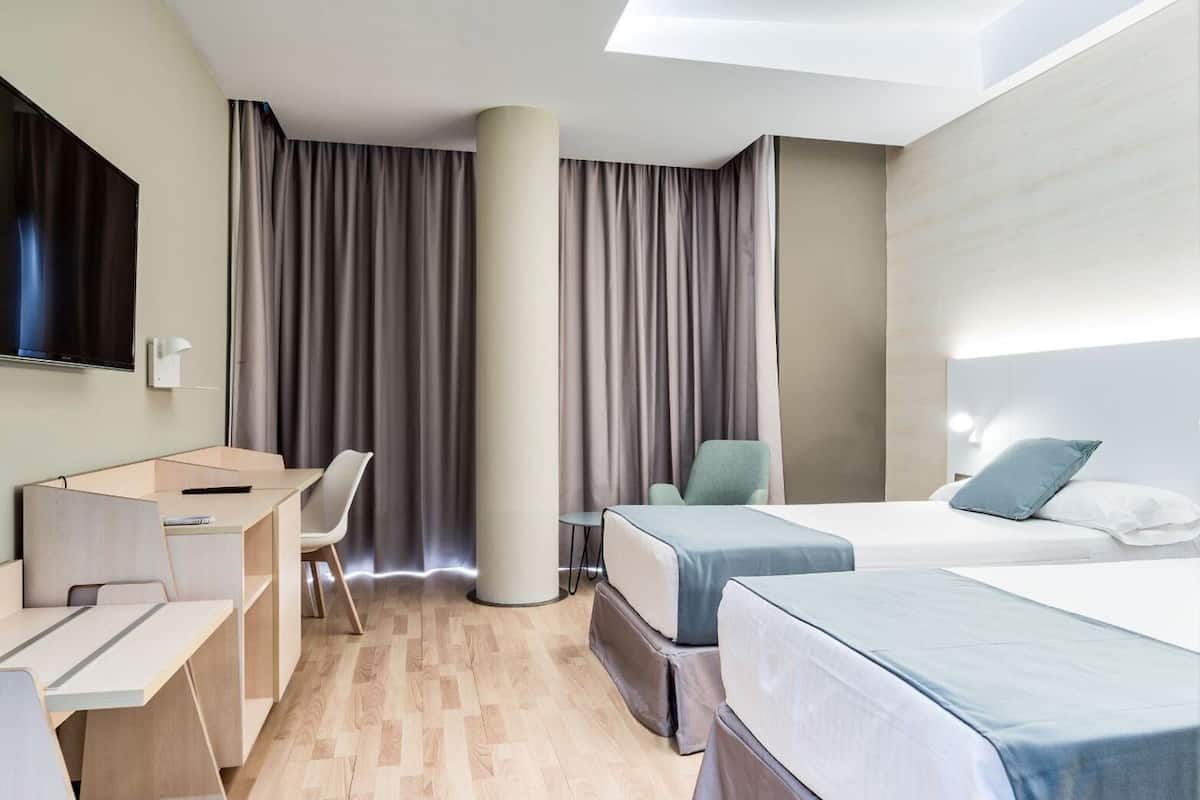 Une chambre d’hôtel avec un lit, un bureau, une chaise, une télévision et une grande fenêtre avec des rideaux.