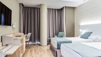 Ett hotellrum med en säng, ett skrivbord, en stol, en tv och ett stort fönster med gardiner.