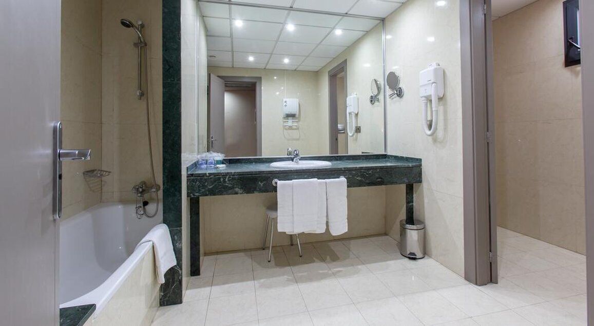 Un bagno moderno con vasca, lavandino e doccia. Asciugamani appesi al muro e un cestino della spazzatura vicino al lavandino.