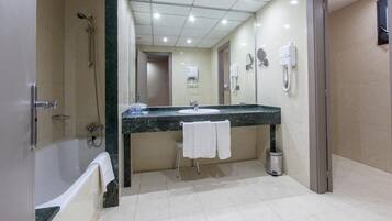 Une salle de bain moderne avec une baignoire, un lavabo et une douche. Des serviettes sont accrochées au mur et une poubelle se trouve à côté du lavabo.