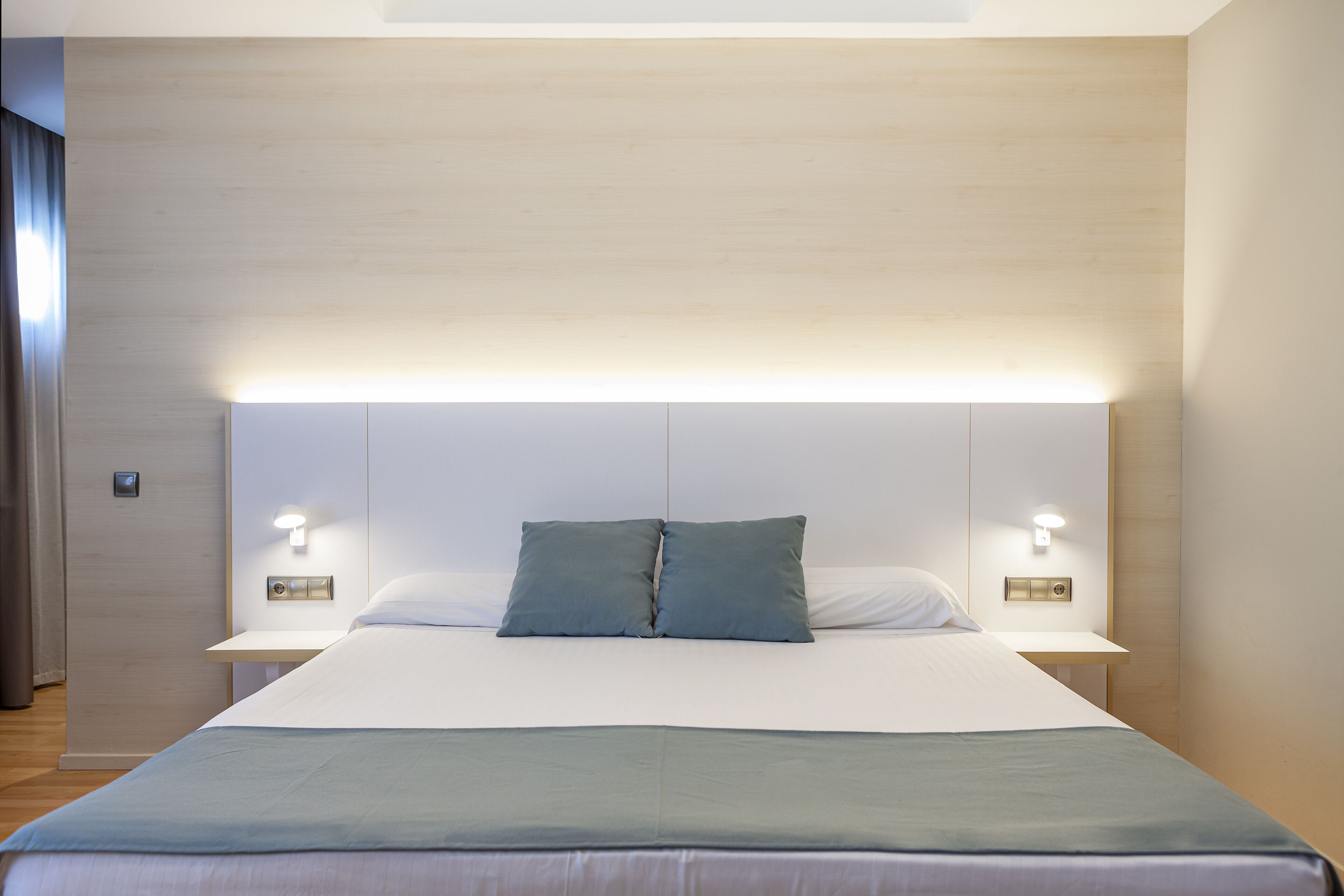 A modern hotel room with a large bed, two bedside tables, and wall-mounted lighting.
