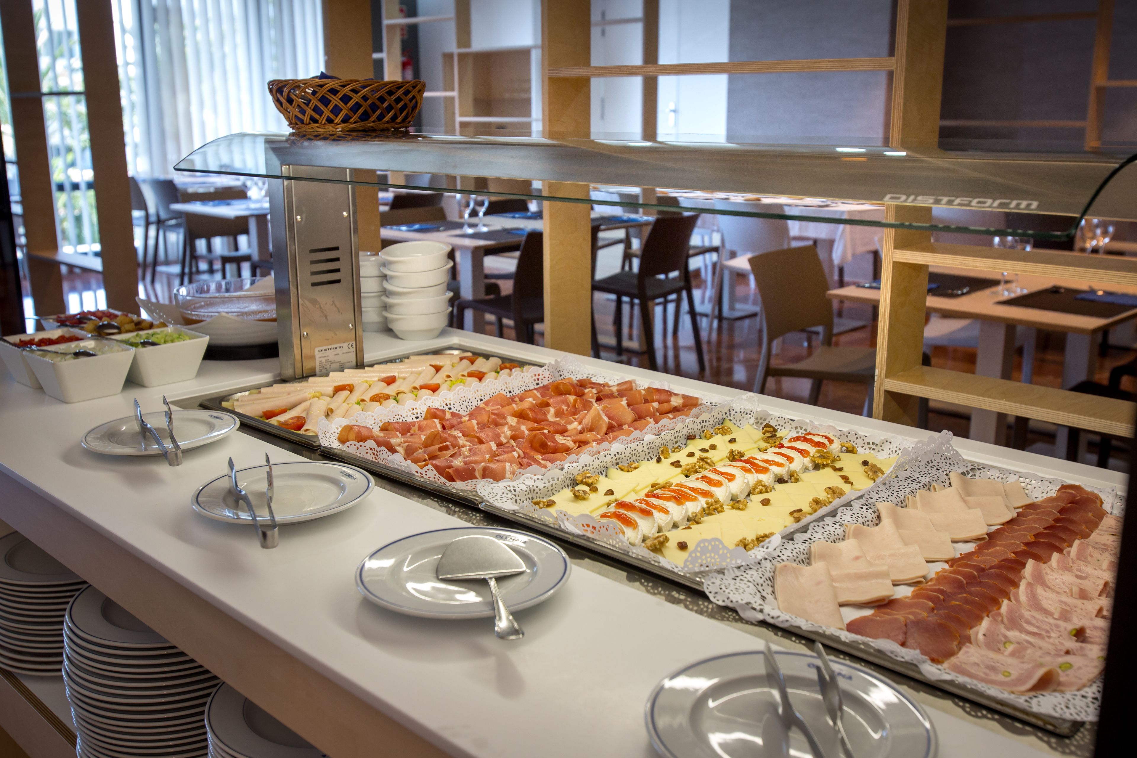 A buffet with various food items, including meats and cheeses, arranged on a glass display.