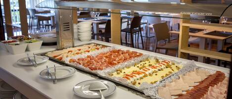 A buffet with various food items, including meats and cheeses, arranged on a glass display.
